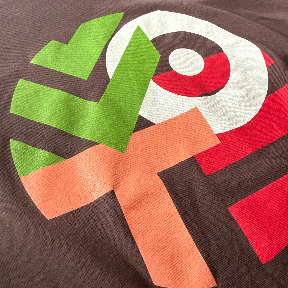 Close-up of a dark brown t-shirt featuring a colorful geometric graphic print in green, orange, red, and white.