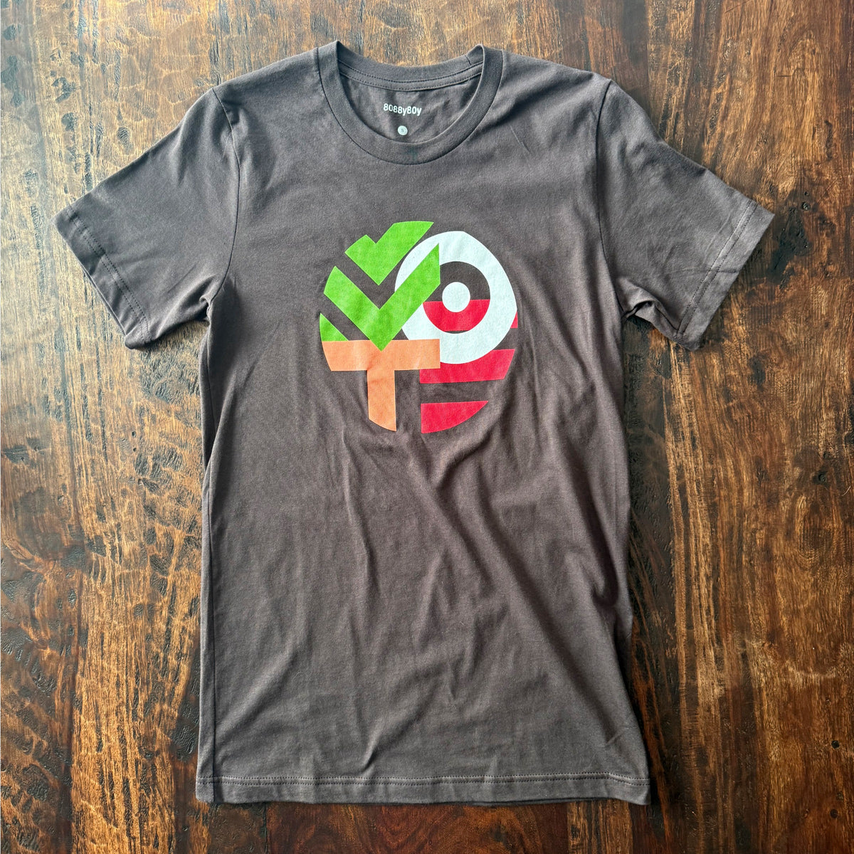 A dark gray crewneck t-shirt with a colorful geometric graphic on the chest, laid flat on a rustic wooden surface.